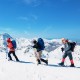 Three hikers using 4-in-1 lightweight terrain snowshoes on snowy mountains, equipped with ski poles and backpacks.